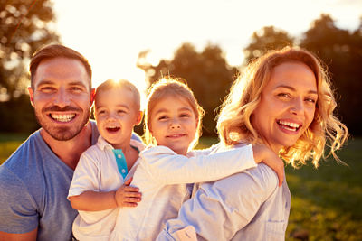 Picture of a young Family of two adults and two young children (boy and girl) smiling outside