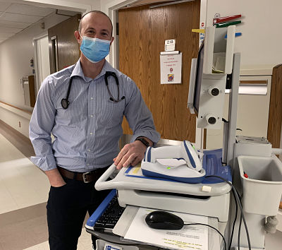 Picture of Dr. Joshua Dobstaff standing in the hallway next to medical machinery and wearing a mask