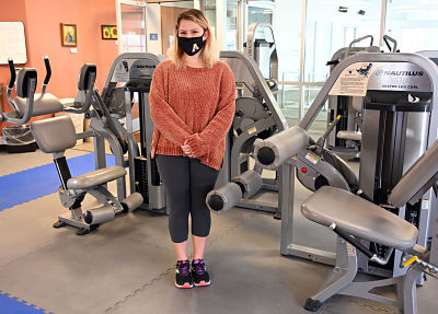 Picture of Anna Mills standing in a gym room, wearing a mask, and looking at the camera