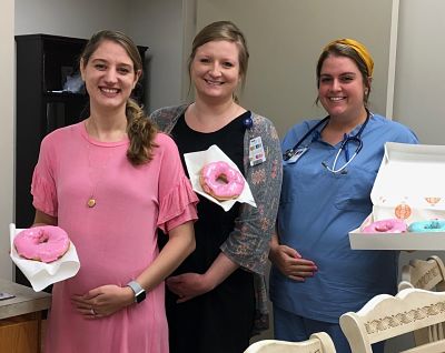 Picture of Mount Jefferson Family Medicine colleagues Jessica Null, Kinsey Jones, and Katie Miller holding their pregnant bellies and doughnuts in another hand. They were all pregnant with boys at the same time.