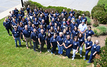 Picture of a group of team members standing outside in the grass and looking up and smiling.