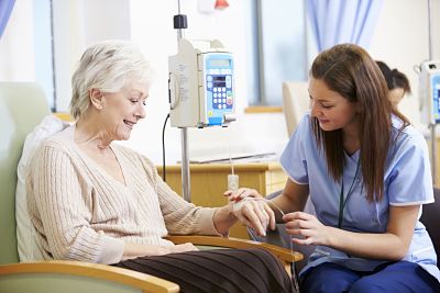 Picture of an elderly female patient in a chair with a female nurse looking at her hand