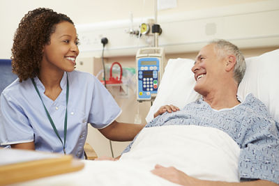 Picture of a Female nurse sitting bedside with a male patient in a hospital bed smiling at each other