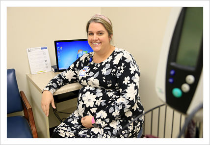 Picture of Katie Miller, FNP-C of Mount Jefferson Family Medicine, sitting down in a patient room smiling. She is now offering telehealth appointments for patients