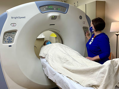 Picture of a female patient getting a CT Scan done while a Medical Staff assists her in the process