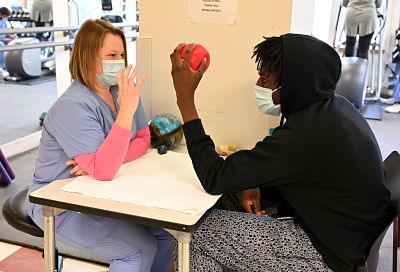 Picture of a man holding an orange ball while nurse shows him how to use it for therapy