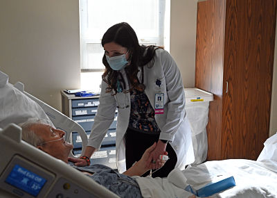 Picture of Dr. Caitlin Sullivan checking on an eldlery patient that is lying down in a swing bed.