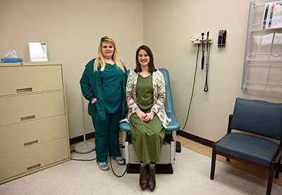 Picture of Nurse Practitioner Jessica Null, standing next to a female patient that is sitting down on an examine chair. They are both smiling.