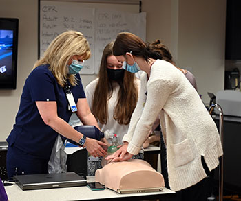 Camp Med students learn how to do CPR on a mannequin with the guidance of a registered nurse.