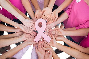 Circle of hands holding a oink breast cancer ribbon.
