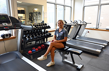 Photo of female athletic trainer sitting on a weight bench in a workout room.
