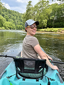 Photo of female sitting in a kayak on the river looking back toward the camera.