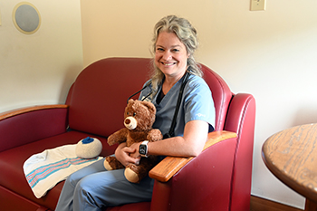 Picture of speech language pathologist sitting on a couch in a labor and delivery room holding a teddy bear.